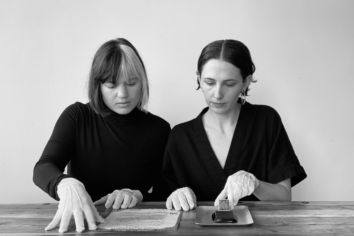 A black and white photo of two women sitting at a table wearing white gloves and signing a marriage certificate.