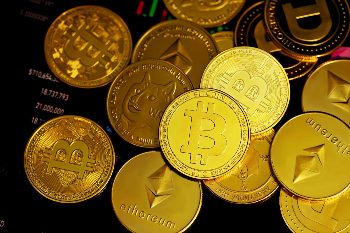 Physical gold coin representations of cryptocurrencies including Bitcoin, Ethereum, DogeCoin, and more against a black background.
