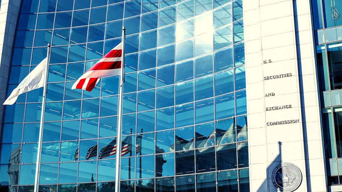 A concrete and glass building sit behind two flags on a sunny day.