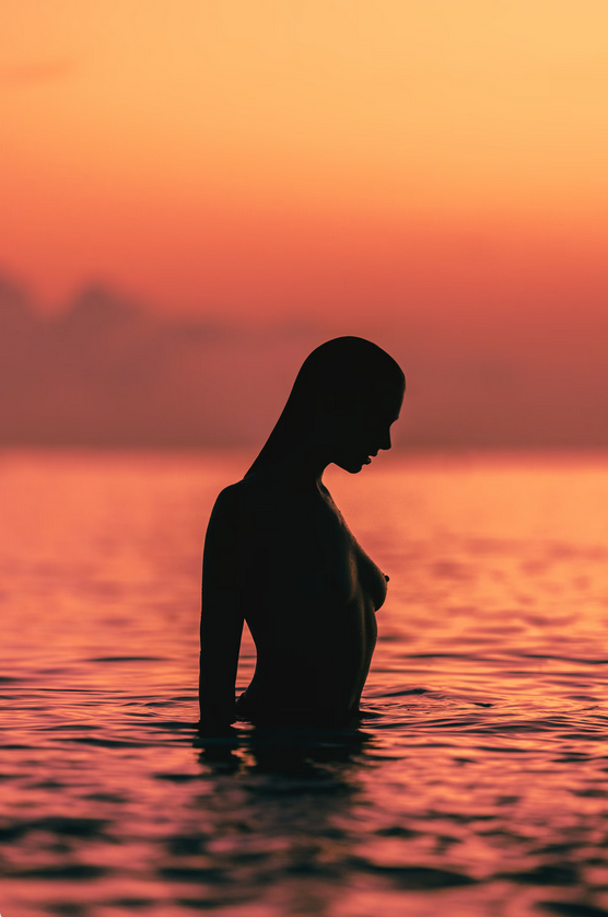 A silhouette of a nude woman in the sea.