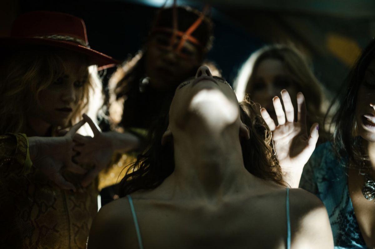 A group of women in a shadowy environment with their hands and heads tilted up and backward.
