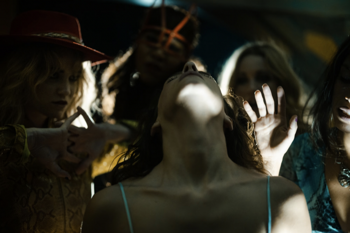 A group of women in a shadowy environment with their hands and heads tilted up and back.