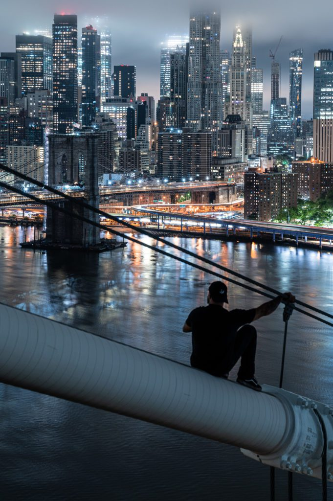 man sits on bridge in silhouette looking out at a city